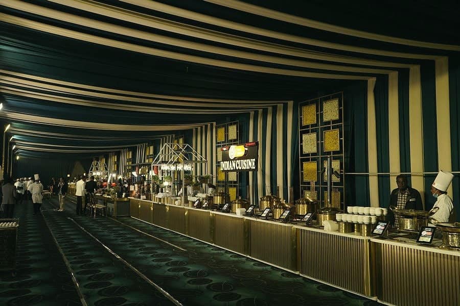 A long buffet counter under a striped tent, staffed by chefs