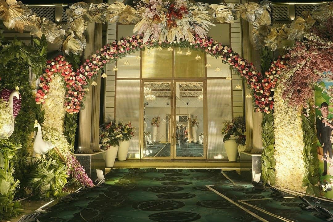 A floral archway with peacock sculptures framing a lit glass entrance