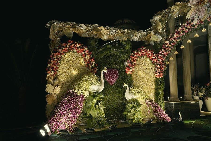 A façade covered in flowers with swan sculptures and a portrait of the couple