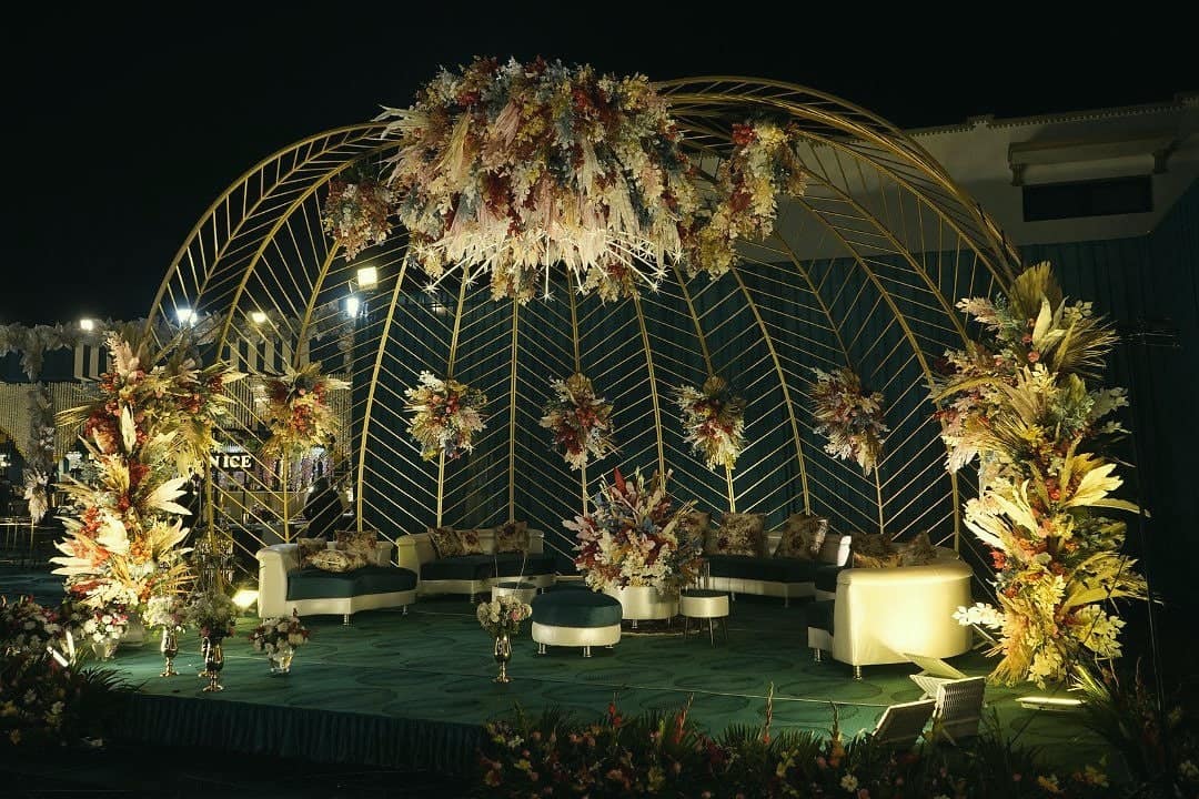 A gold domed pergola dressed in pampas and flowers, with lounge seating beneath