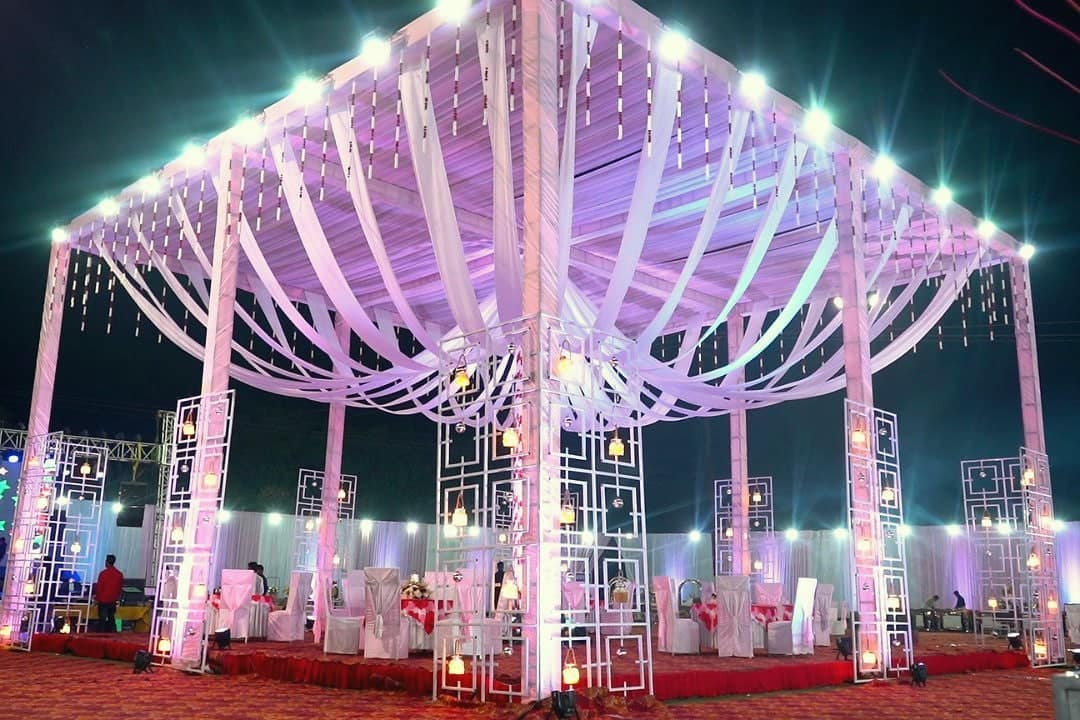 A wedding mandap draped in white fabric and lit with fairy lights
