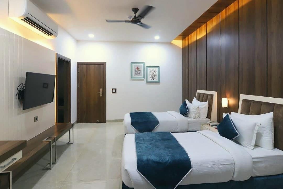 A guest room with twin beds, a TV wall and armchairs